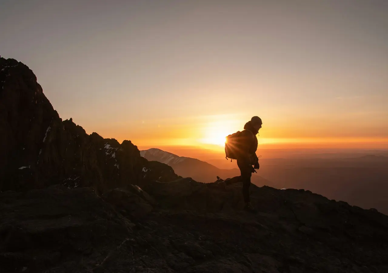 A hiker silhouetted on a rocky summit at sunset