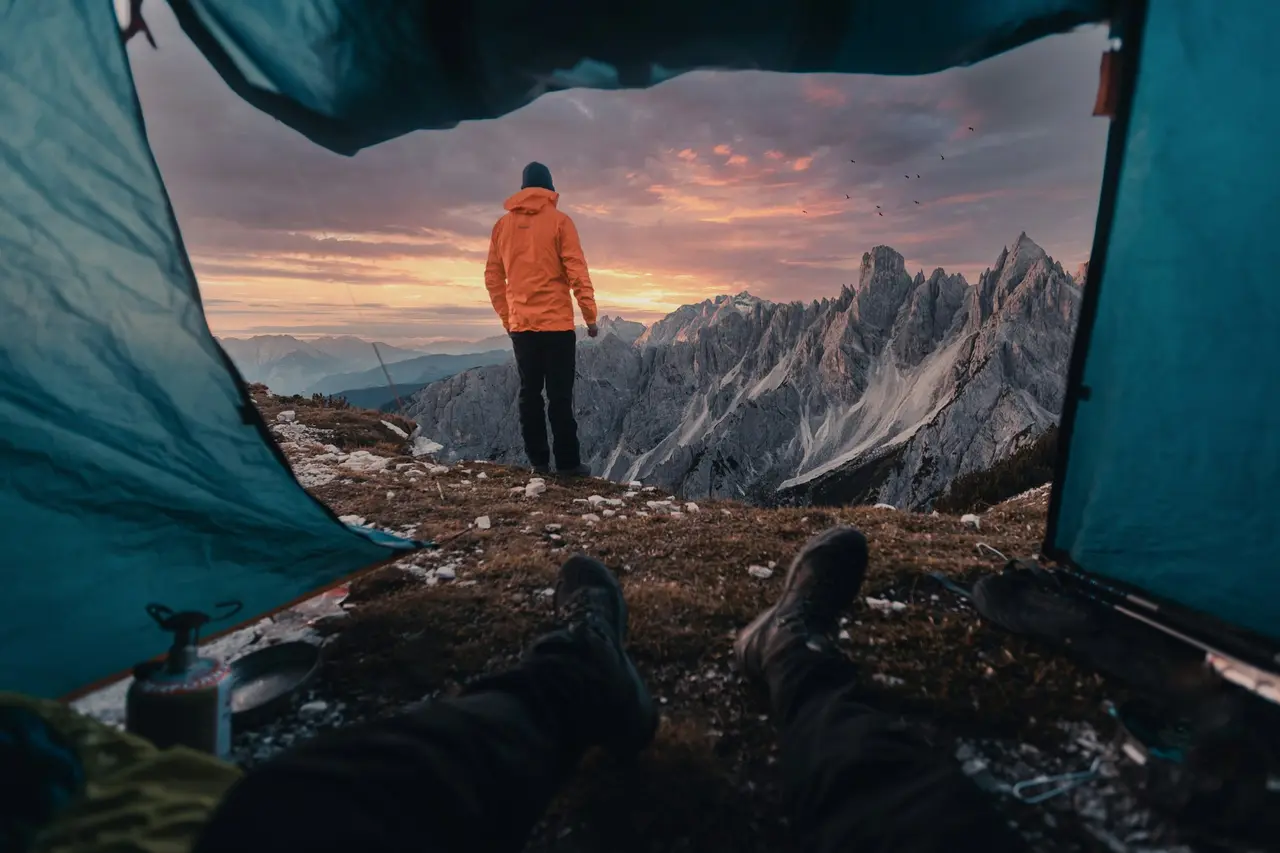 A hiker standing outside a tent door facing the mountains