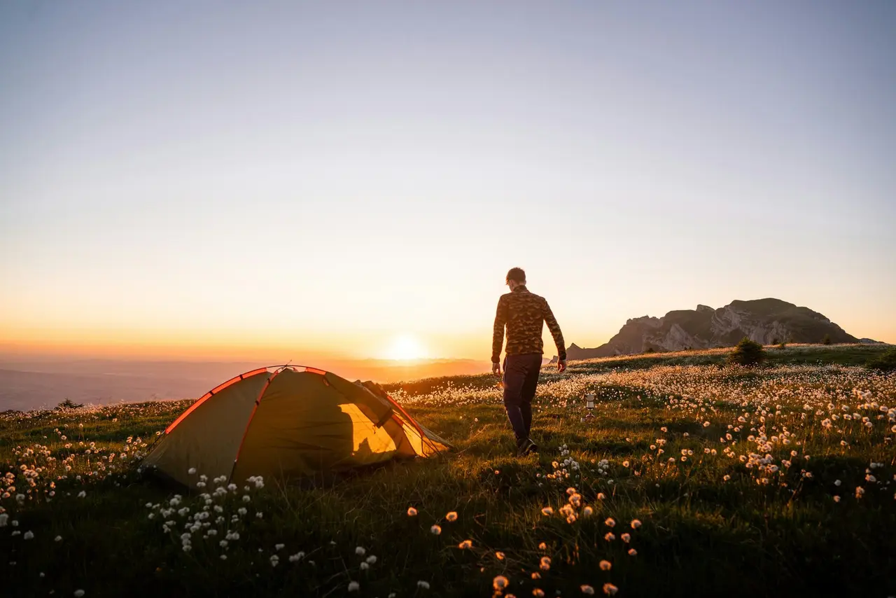 A hiker walking past a tent as the sun sets